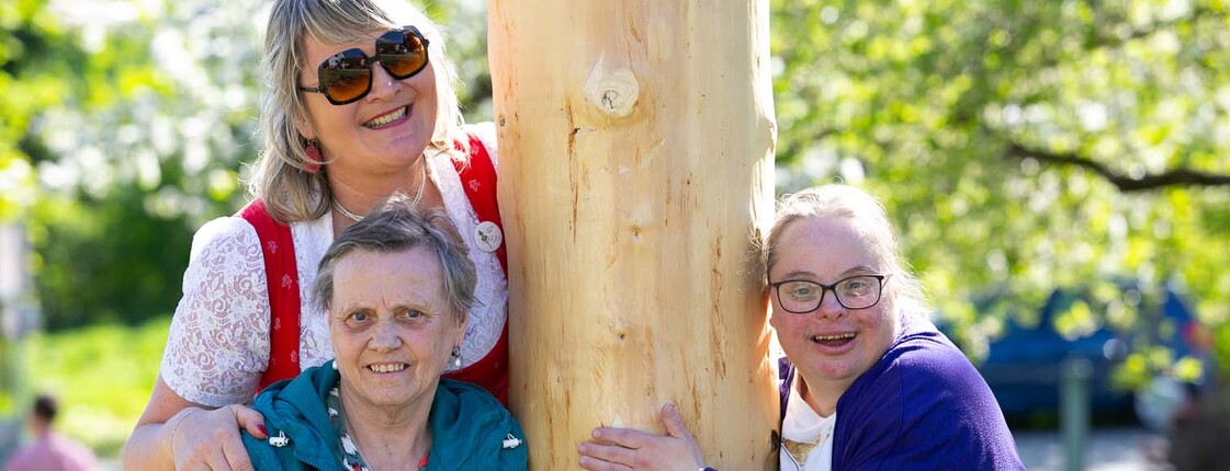 Drei Personen halten einen Maibaum 