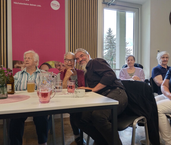 Bewohner*innen sitzen an einem Tisch mit Getränken und Blumen und verbringen gemeinsam Zeit bei der Muttertagsfeier.