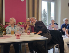 Bewohner*innen sitzen an einem Tisch mit Getränken und Blumen und verbringen gemeinsam Zeit bei der Muttertagsfeier.