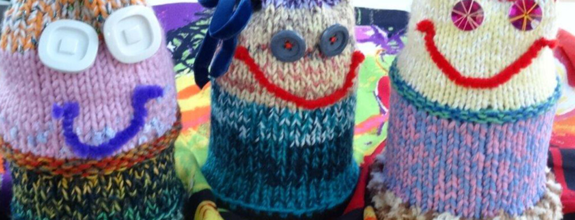 Verzierte, farbige Spendengläser. Man hat den Gläsern Gesichter aufgeklebt. Sie sind mit Stoff umhüllt. 