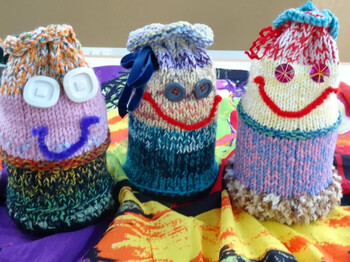 Verzierte, farbige Spendengläser. Man hat den Gläsern Gesichter aufgeklebt. Sie sind mit Stoff umhüllt. 