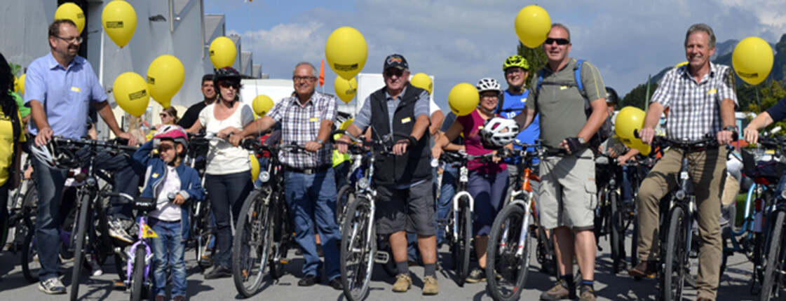 Um die 10 Menschen auf Rädern stehen nebeneinander im Freien unter blauem Himmel. 