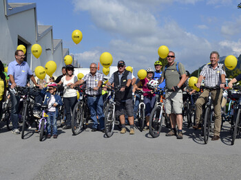 Um die 10 Menschen auf Rädern stehen nebeneinander im Freien unter blauem Himmel. 