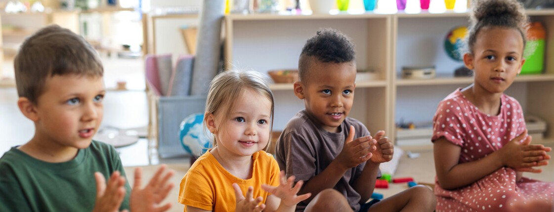 Kinder sitzen in einer Gruppe im Raum und klatschen mit den Händen.