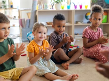 Kinder sitzen in einer Gruppe im Raum und klatschen mit den Händen.