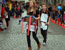 Eine junge Erwachsene und ein junger Erwachsener tragen schwarze Kleidung mit einer weißen Schürtze. Sie präsentieren diese Kreation in der feldkircher Innnenstadt Passanten am carla Reuse Day. 