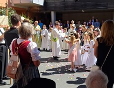 Vor dem Pflegewohnhaus spendet ein Geistlicher den Erstkommunionskindern im Rahmen einer feierlichen Prozession den Segen, während Bewohnerinnen und Bewohner das Geschehen aufmerksam verfolgen.