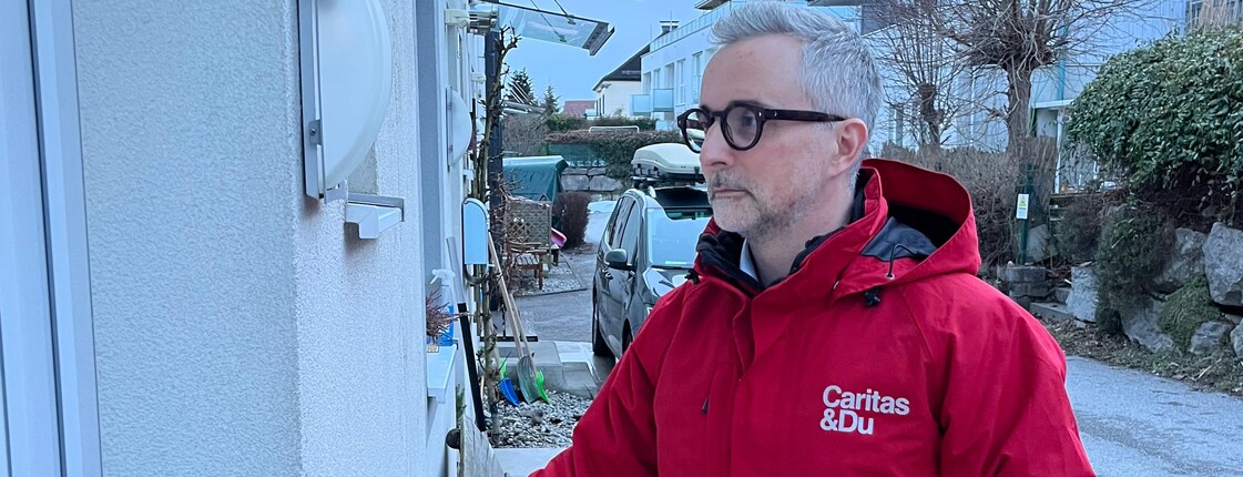 Ein Mann mit Caritas Jacke läutet an einer Haustür