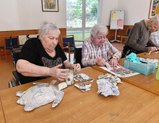 Mehrere Bewohner*innen gestalten mit Papierstreifen und Kleister Papiermaché-Figuren an einem Tisch im Aufenthaltsraum.