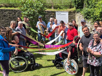 Gruppe von Teilnehmenden hält bunte Bänder im Kreis; gemeinsames Symbol für Pfingsten und Verbindung zwischen Gott und Mensch im Freien