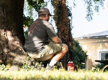 Person sitzt bei Sommerhitze im Schatten eines Baumes, daneben eine Trinkflasche auf einer Wiese.