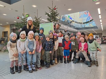 Eine Gruppe Kindergartenkinder steht vor einem Christbaum in einem Einkaufscenter.