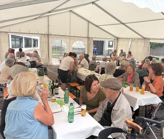 Zahlreiche Gäste sitzen an gedeckten Tischen im Festzelt und verbringen den Nachmittag gemeinsam.