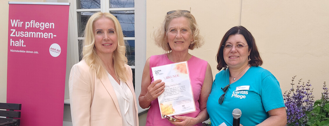 Zwei Personen überreichen im Freien eine Dankesurkunde für freiwilliges Engagement an eine Freiwillige im Caritas‑Haus Elisabeth