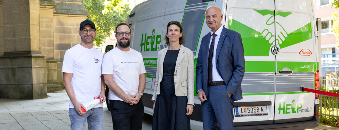 Drei Männer und eine Frau stehen vor einem Kleinbus mit der Aufschrift Help-Mobil.