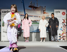 carla Modeschau: Auch Kinder bekommen die Möglichkeit ihre Persönlichkeit mit Gewand auszudrücken und es anderen stolz zu präsentieren: Ein junges Mädchen von etwa sechs Jahren läuft mit einem weißen Bademantel und einem Stofftier in der Hand über den Laufsteg. Im Hintergrud sind erwachsene Models die voller Freude die Performance des Mädchen genießen. 