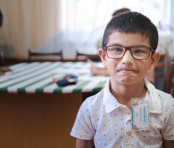 Nahaufnahme eines kleinen jungen mit schwarzen Haaren und Brille, der direkt in die Kamera blickt.