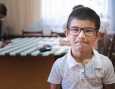 Nahaufnahme eines kleinen jungen mit schwarzen Haaren und Brille, der direkt in die Kamera blickt.