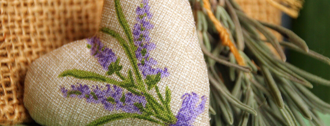 Stoffherz mit Lavendelmotiv neben getrockneten Kräutern.