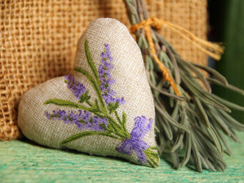 Stoffherz mit Lavendelmotiv neben getrockneten Kräutern.