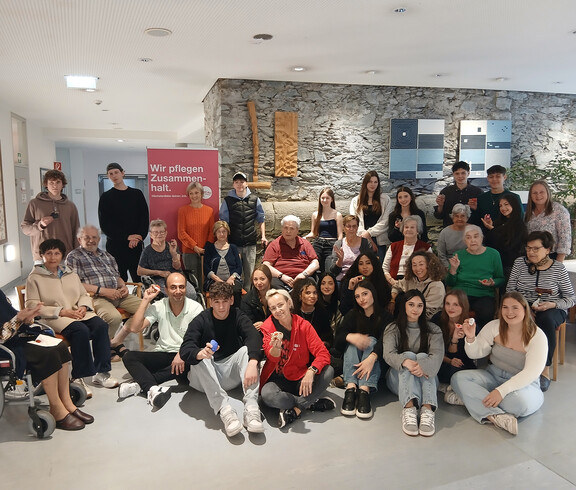 Gruppenfoto von HLW- und Erasmus-Schülerinnen mit Bewohnerinnen im Haus Martha vor Banner „Wir pflegen Zusammenhalt.“