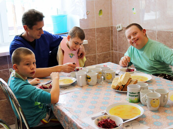 Kinder im Kinderdorf Gomel nehmen gemeinsam mit einem Betreuer ihre Mahlzeiten ein, wobei einige Kinder unterstützt werden.