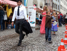 Sowohl ein junger Erwachsener als auch Kinder in Tracht gehen durch die feldkircher Innenstadt um ihre modische Kleidung zu präsentieren. 