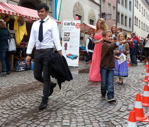 Sowohl ein junger Erwachsener als auch Kinder in Tracht gehen durch die feldkircher Innenstadt um ihre modische Kleidung zu präsentieren. 