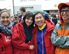Vier Caritas Mitarbeiterinnen nahmen bei einem Laufwettbewerb teil. Sie stehen in der feldkircher Innenstadt zu einem Gruppnfoto zusammen. Drei tragen eine rote Regenjacke. Die andere eine orange graue. Im Hintergrund sind etliche Menschen in einer Masse versammelt. 
