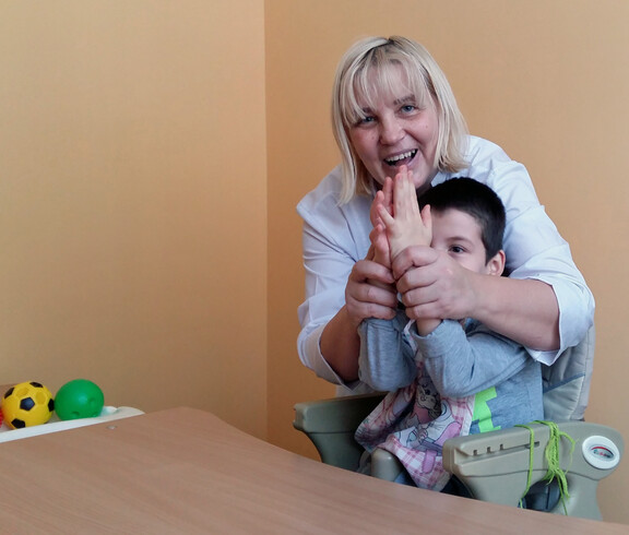 Eine Therapeutin arbeitet mit einem Kind im Kinderdorf Gomel an einer Therapie, indem sie mit ihm Hände schüttelt und spielerische Übungen macht.