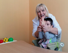 Eine Therapeutin arbeitet mit einem Kind im Kinderdorf Gomel an einer Therapie, indem sie mit ihm Hände schüttelt und spielerische Übungen macht.