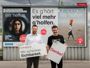David Edlinger, Geschäftsführer PSG Poster Service GmbH und Caritasdirektor Ernst Sandriesser vor Caritas-Plakaten halten Schilder mit „Wir schenken Sichtbarkeit“ und „Danke!“.