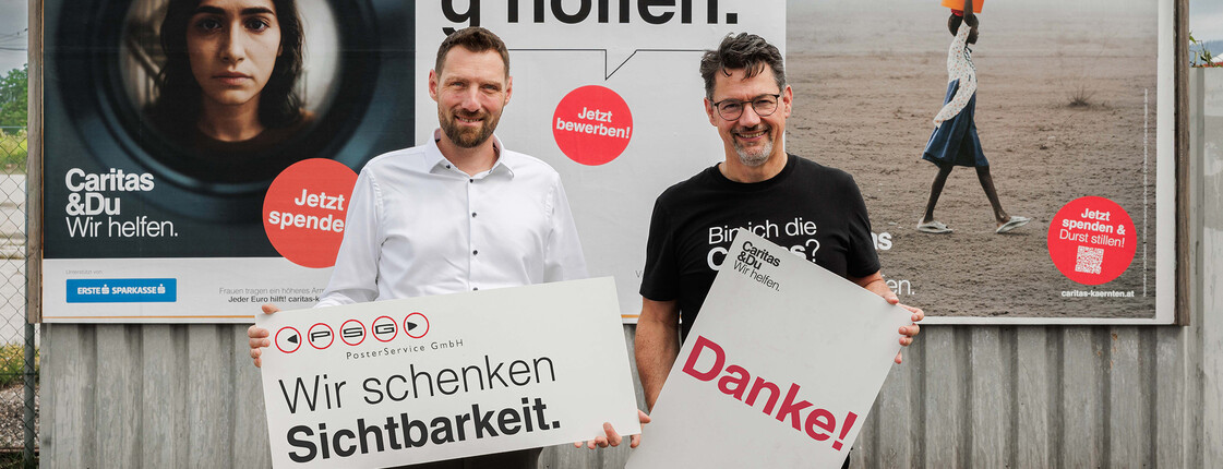 David Edlinger, Geschäftsführer PSG Poster Service GmbH und Caritasdirektor Ernst Sandriesser vor Caritas-Plakaten halten Schilder mit „Wir schenken Sichtbarkeit“ und „Danke!“.
