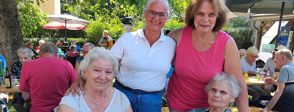 Bewohner*innen und Angehörige versammeln sich beim Grillfest an einer gedeckten Festtafel im Garten.