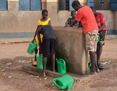 Ein paar Burschen aus dem Südsudan stehen mit Gießkannen an einem Wasserhahn. 