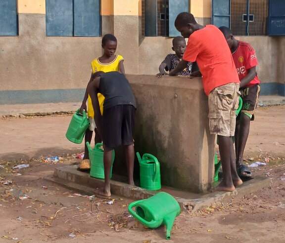 Ein paar Burschen aus dem Südsudan stehen mit Gießkannen an einem Wasserhahn. 