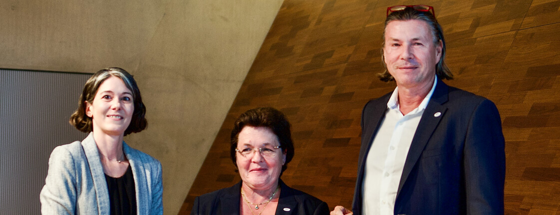 Drei Personen halten eine Urkunde in der Hand