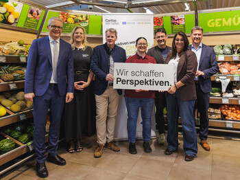 Gruppe in Supermarkt hält Schild „Wir schaffen Perspektiven“ für Caritas-Qualifizierungsprojekt „perspektiven.werk“.