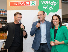 Drei Personen sprechen mit Mikrofon vor SPAR-Logo bei Eröffnung und stehen vor Getränkeregal.