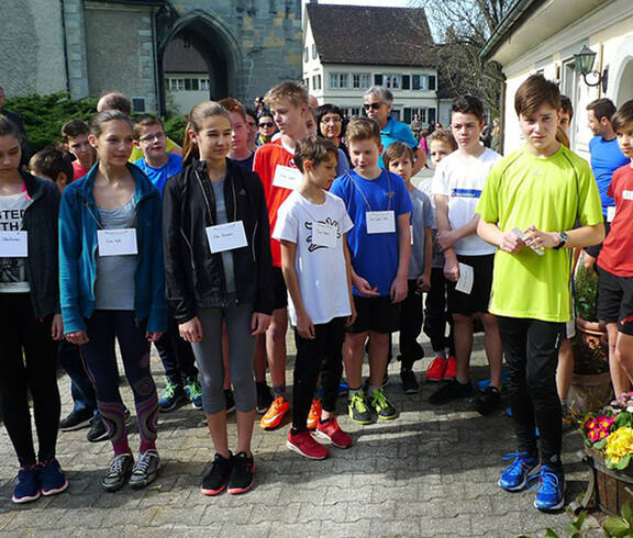 Junge Burschen und Mädchen versammeln sich für ein Gruppenfoto. Sie tragen alle Sportkleidung und ein Namensschild.