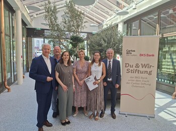 Sechs Personen stehen in heller Halle neben Banner „Du & Wir-Stiftung“ von Caritas und BKS Bank, Fokus auf Förderung der Hospizbegleitung.