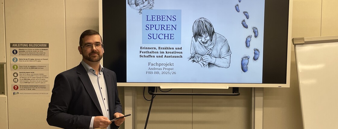 Mann mit dunklen kurzen Haaren im Anzug mit weißem Hemd seitlich links von einem Präsentationsbildschirm.