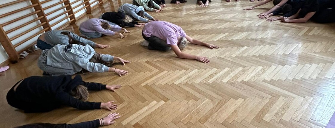 Im Turnsaal machen viele Schüler*innen die Yogaposition des Kindes.