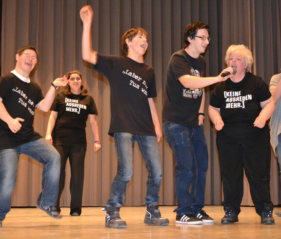 Menschen mit Behinderung tanzen und singen auf einer Bühne. 