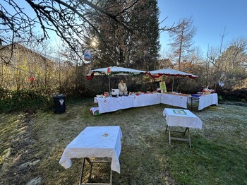 In einem Garten sind Tische mit weißen Tischdecken als Verkaufsstände aufgebaut.