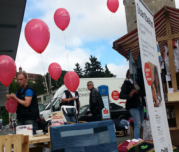 carla stellt in der feldkircher Innenstadt wieder in Stand gesetzte möbel aus. An den Möbel, unter anderem Sessel und Holztische, wurden einige rote Luftballons befestigt. 