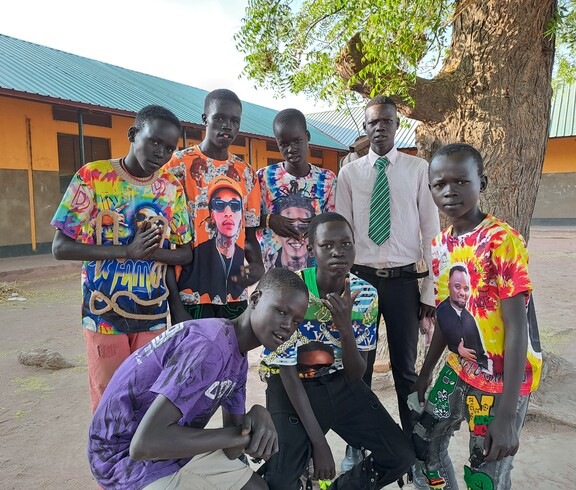 Eine Gruppe junger Südsudanesen posiert unter einem Baum. Alle haben bunte Tshirts an. 