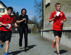 Drei Personen laufen in Sportbekleidung beim Stundenlauf. Eine Frau in der Mitte ganz schwarz bekleidet und zwei Jungs rennen ihr davon.