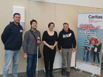 Vier Personen vor einem Plakat.