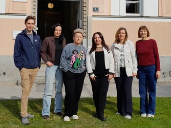 Sechs Personen stehen in einer Reihe vor einem Haus und schauen in die Kamera